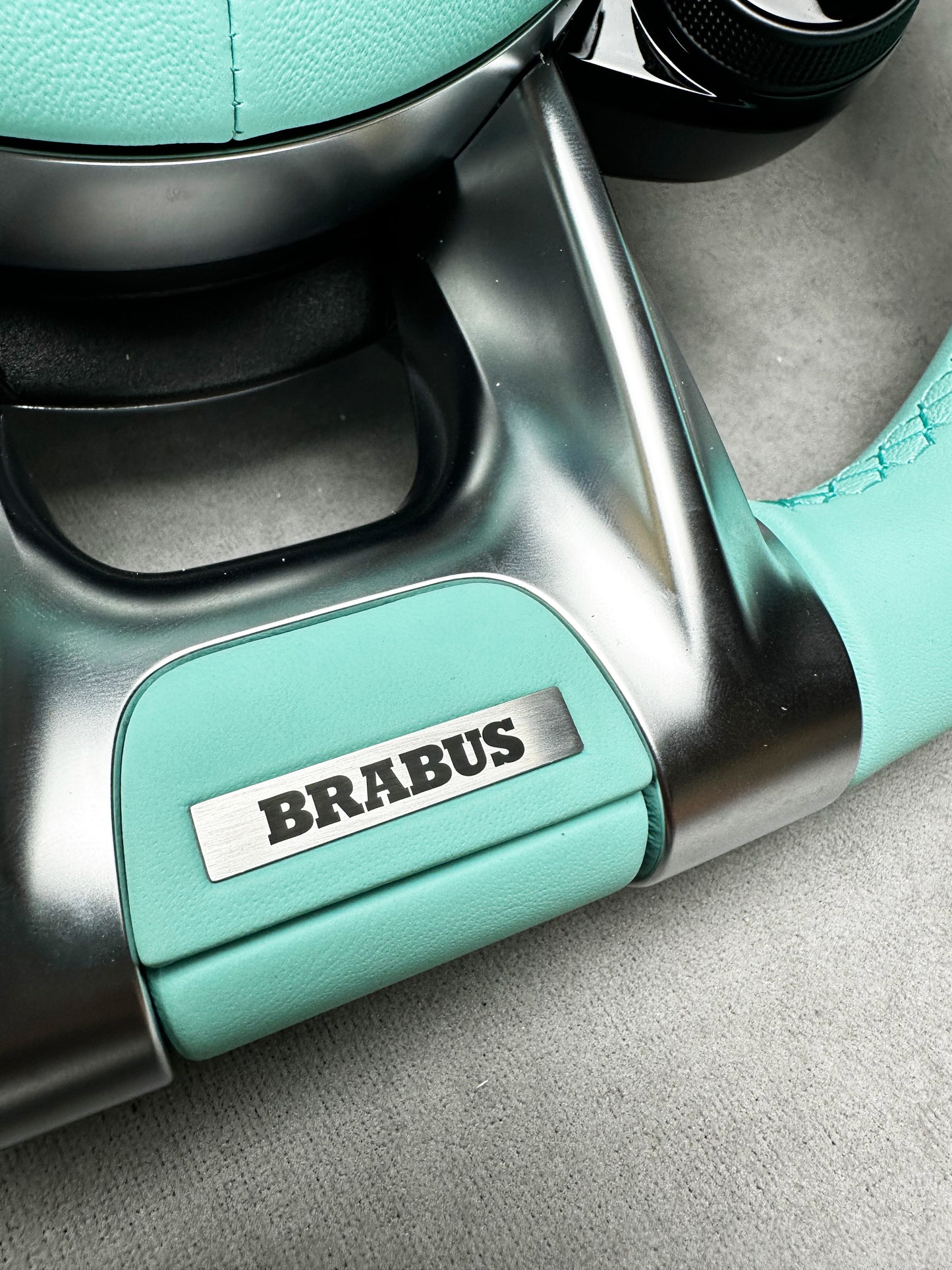 Close-up of Brabus Tiffany Blue interior emblem with metal insert on a Mercedes steering wheel