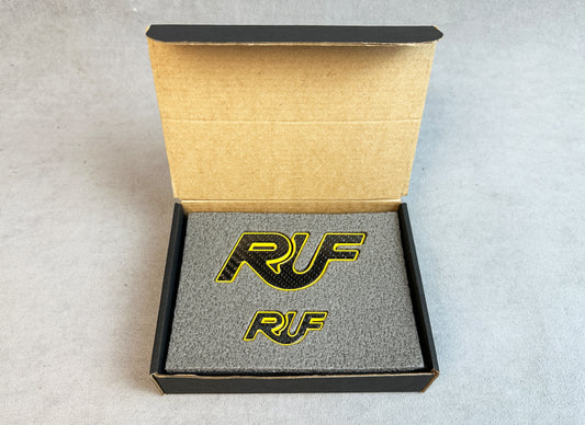 Yellow metal RUF badge on carbon background for Porsche 997