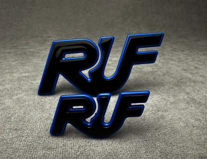 Close-up of two-piece RUF emblem badge set in black and blue metal finish