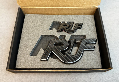 Pair of solid RUF carbon emblems displayed