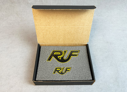Yellow metal RUF badge on carbon background for Porsche 997