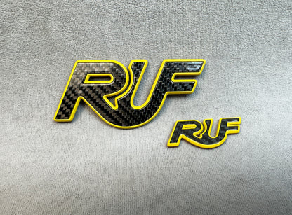 Two-piece set of RUF carbon yellow metal badges on display